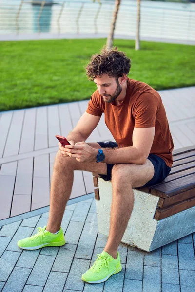 Hombre adulto joven usando un teléfono celular moderno en el parque . — Foto de Stock