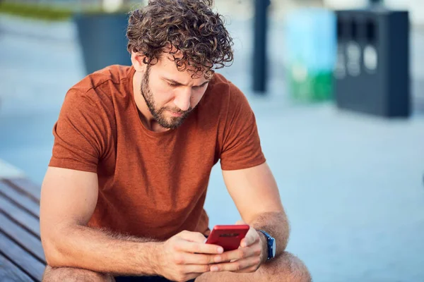 Junger erwachsener Mann mit modernem Handy im Park. — Stockfoto