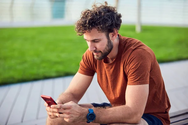 Homem adulto jovem usando celular moderno no parque . — Fotografia de Stock