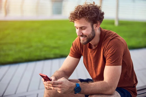 Hombre adulto joven usando un teléfono celular moderno en el parque . —  Fotos de Stock