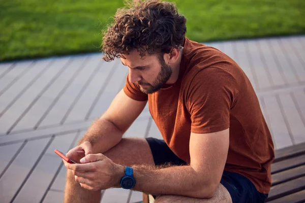 Homem adulto jovem usando celular moderno no parque . — Fotografia de Stock