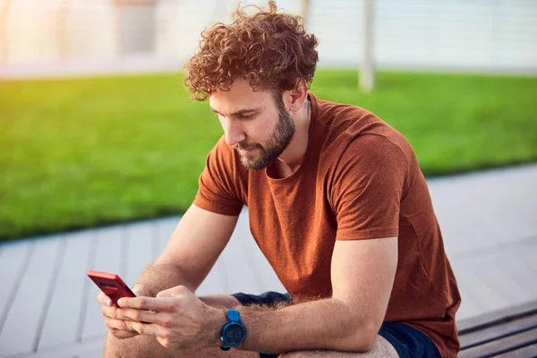 Homem adulto jovem usando celular moderno no parque . — Fotografia de Stock