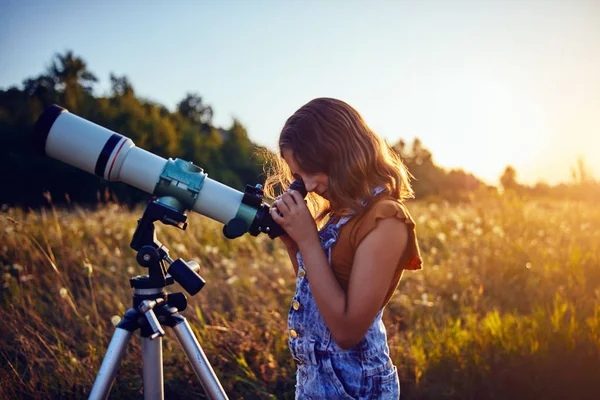 Niña usando telescopio en la naturaleza para explorar el universo . —  Fotos de Stock