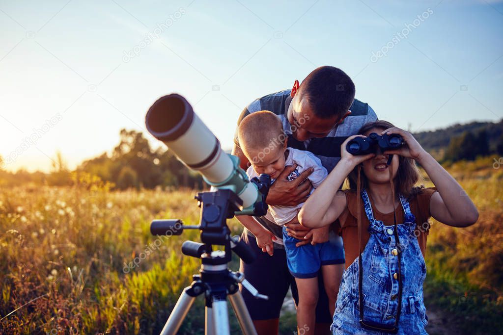 Father, daughter and son observing the sky with a telescope.