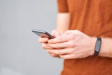 Genç adam gri renkli bir duvarın yanında akıllı telefon kullanıyor.