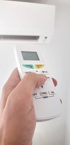 Modern luftkonditionering enhet med en hand som håller en fjärrkontroll. — Stockfoto