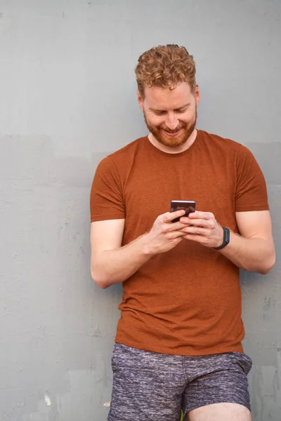 Junger Mann benutzt Smartphone in der Nähe einer schlampig bemalten grauen Stadtmauer — Stockfoto