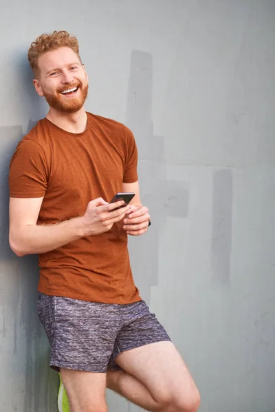 Hombre joven usando teléfono inteligente cerca de una pared urbana gris pintada descuidada — Foto de Stock