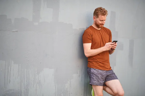 Hombre joven usando teléfono inteligente cerca de una pared urbana gris pintada descuidada — Foto de Stock
