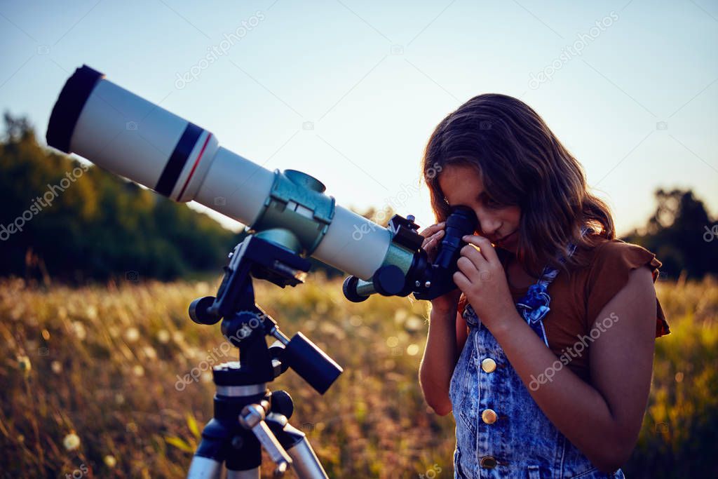 Little girl using telescope in nature to explore the universe.