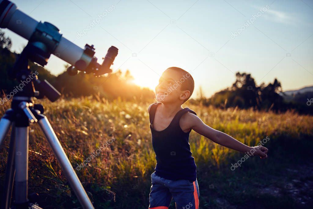 Little boy using telescope in nature to explore the universe.