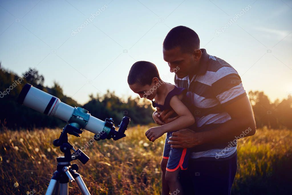 Father and son observing the sky with a telescope.