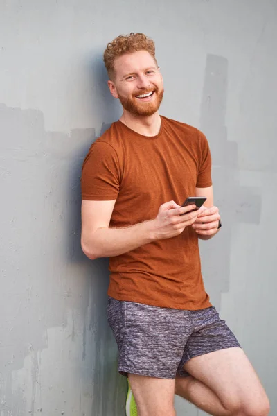 Hombre joven usando teléfono inteligente cerca de una pared urbana gris pintada descuidada — Foto de Stock