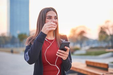 Modern young woman with cellphone making pause during jogging / 