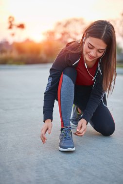 Şehir parkında koşu ayakkabısı bağlayan genç modern bir kadın..
