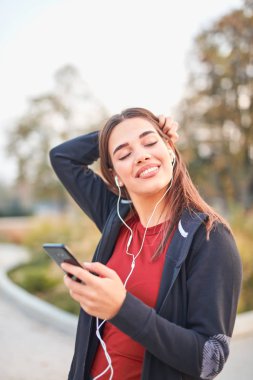Modern young woman with cellphone making pause during jogging / 