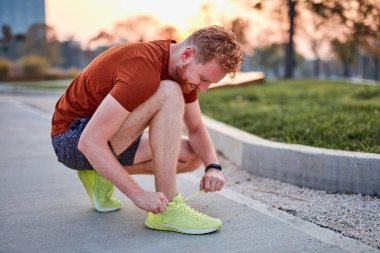 Şehir parkında koşu ayakkabısı bağlayan genç modern bir adam..