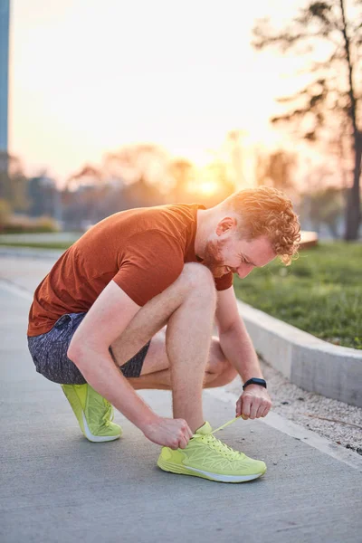 Joven hombre moderno atando zapatillas en un parque urbano . — Foto de Stock