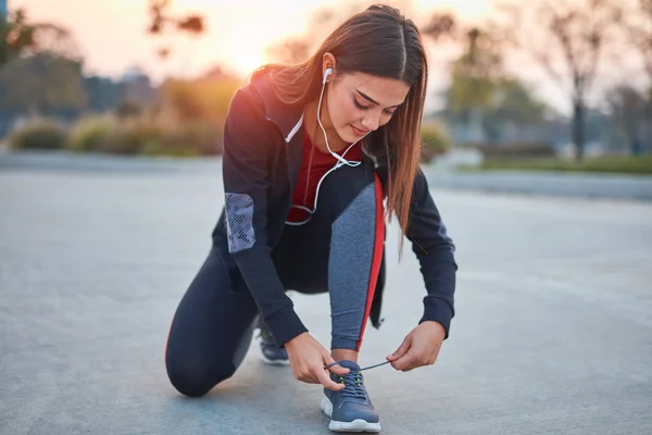 Jeune femme moderne attachant des chaussures de course dans un parc urbain . — Photo