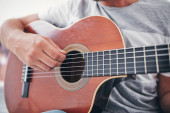 Muž hraje na akustickou kytaru v obývacím pokoji.