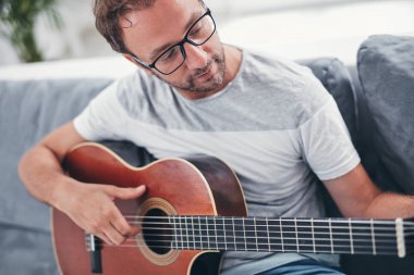 Adam oturma odasında akustik gitar çalıyor..