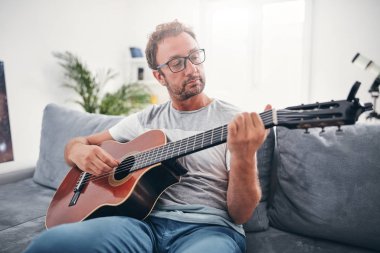 Adam oturma odasında akustik gitar çalıyor..