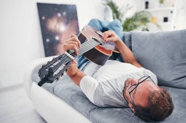 Adam oturma odasında akustik gitar çalıyor..