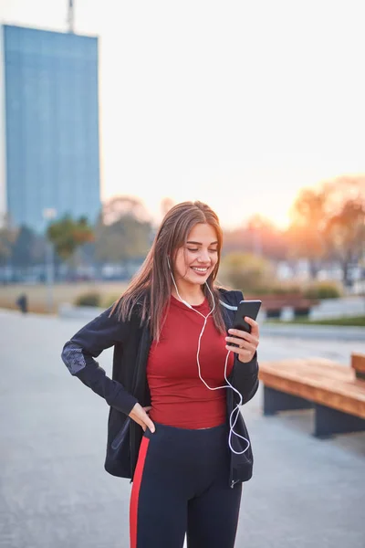 Современная молодая женщина с мобильным телефоном делает паузу во время пробежки. — стоковое фото