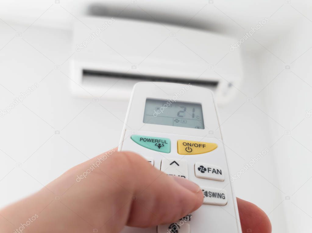 Modern airconditioner unit with a hand holding a remote.