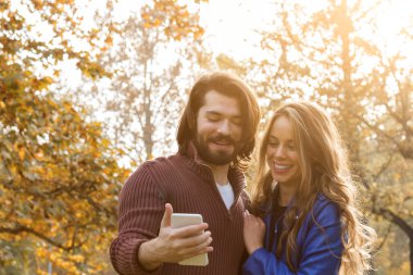 Genç çift sonbahar renkli park'cep telefonu kullanma.