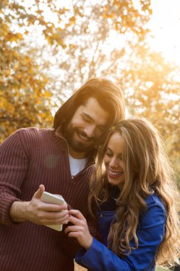 Genç çift sonbahar renkli park'cep telefonu kullanma.
