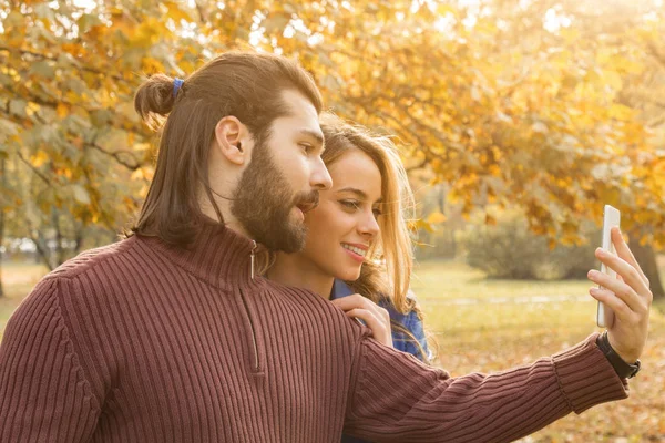 Fiatal pár őszi színes park mobiltelefon segítségével. — Stock Fotó