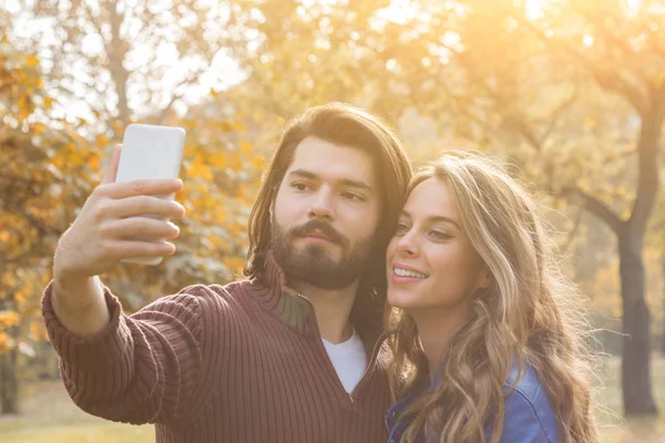 Giovane coppia utilizzando il cellulare in autunno colorato parco . — Foto Stock