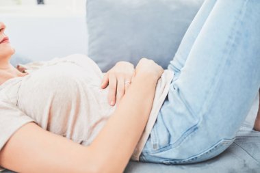 Kanepede yatarken mide sorunları olan bir kadın..