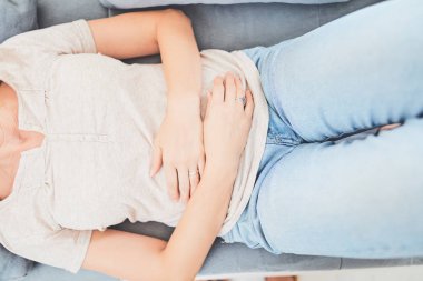 Kanepede yatarken mide sorunları olan bir kadın..