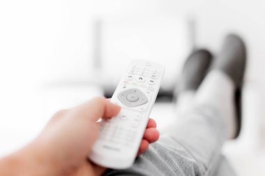 Oturma odasında bacakları masanın üstünde televizyona bakan bir adam..