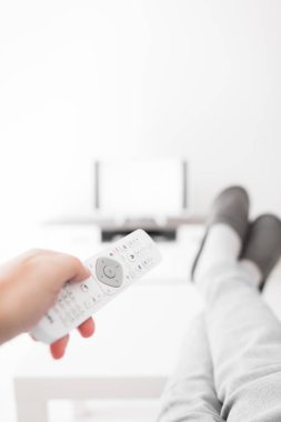 Oturma odasında bacakları masanın üstünde televizyona bakan bir adam..