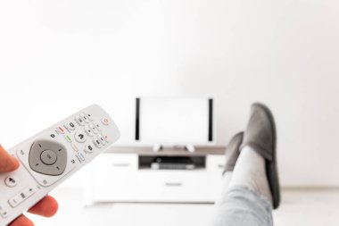 Oturma odasında bacakları masanın üstünde televizyona bakan bir adam..