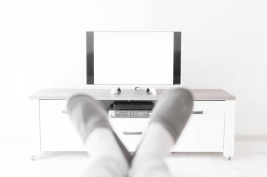 Oturma odasında bacakları masanın üstünde televizyona bakan bir adam..