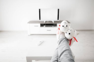 Oturma odasında bacakları masanın üstünde televizyona bakan bir kadın..