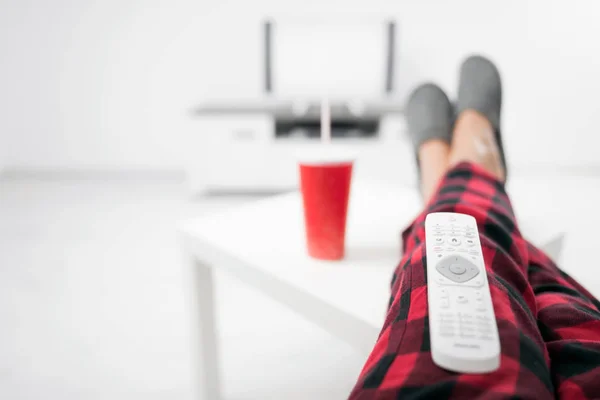 Man drinkt frisdrank en kijkt tv met benen op tafel. — Stockfoto