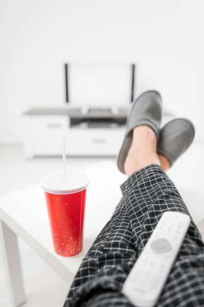 Hombre bebiendo jugo de soda y mirando televisión con piernas en la mesa — Foto de Stock