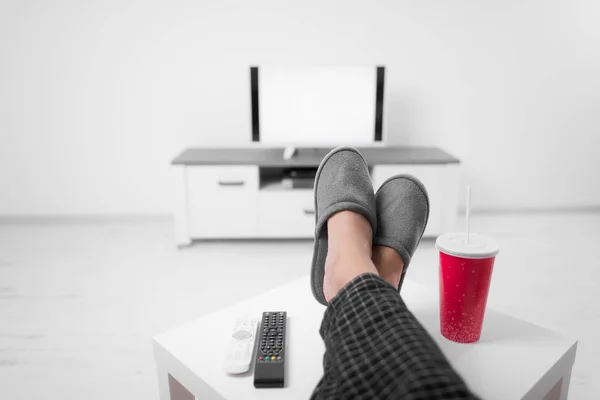 Чоловік п'є содовий сік і дивиться телевізор з ногами на столі — стокове фото