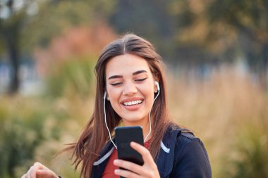 Modern young woman with cellphone making pause during jogging / 