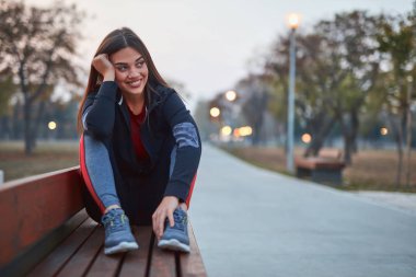 Genç bir kadın, şehir parkında egzersiz yaptıktan sonra duraklıyor..
