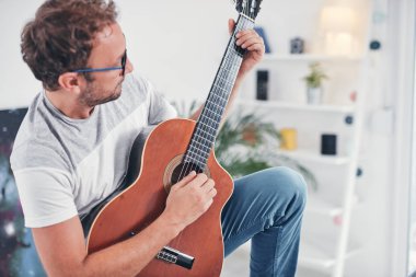 Adam oturma odasında akustik gitar çalıyor..