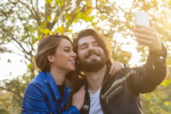 Молода пара використовує мобільний телефон в осінньому кольоровому парку . — стокове фото