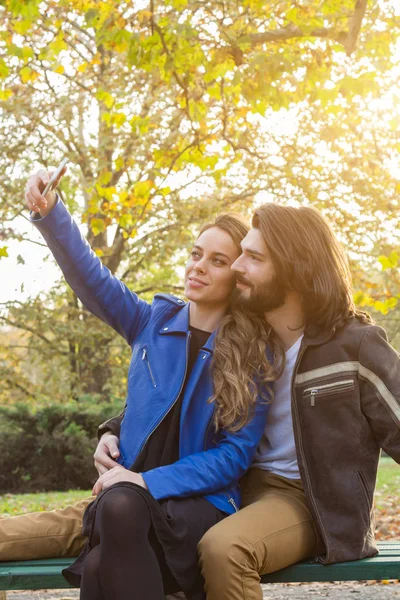 Junges Paar benutzt Handy im herbstlich gefärbten Park. — Stockfoto