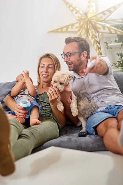 Young parents watching TV with baby boy and a dog.