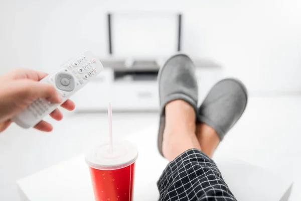 Hombre bebiendo jugo de soda y mirando televisión con piernas en la mesa — Foto de Stock
